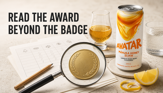 Avatar Elixir beside a magnifying glass, generic award medallion, tasting glass, and blind judging score sheets, with headline reading Read the Award Beyond the Badge.