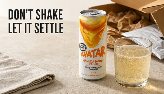 Avatar Elixir can set upright beside a calm sparkling honey drink pour, with delivery packaging behind it and headline text reading DON’T SHAKE LET IT SETTLE.