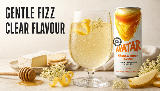 Avatar Elixir can beside a chilled glass with fine gentle bubbles rising through a pale honey drink, with lemon, elderflower, honey, cheese, crackers, and fruit on a warm stone ta...