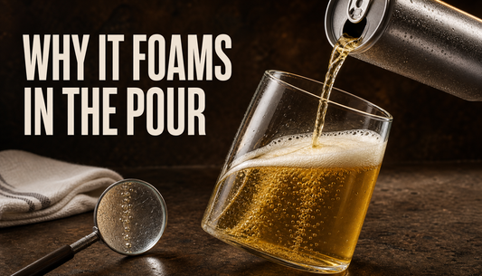 A golden sparkling honey drink pours from an unlabeled chilled can into a tilted glass as bubbles form along the glass wall and collect into a light foam head.